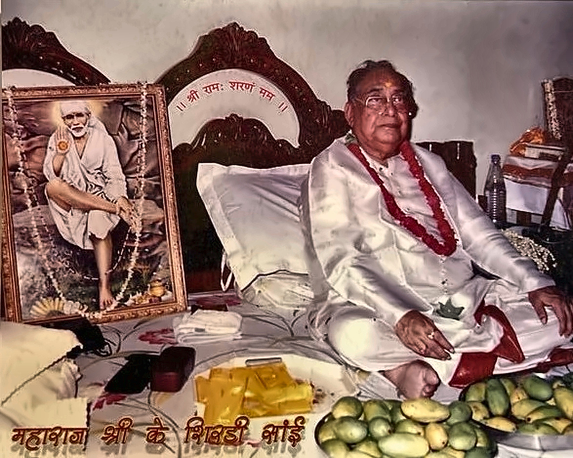 Seated beside a sacred portrait of Shirdi Sai Baba